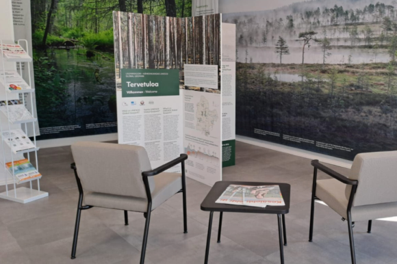 ylieskuva infopisteen tiloista, kuvassa esiteteline, kaksi tuolia, pieni pöytä ja taustalla isot kuvat geoparkista