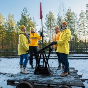 iloisia henkilöitä keltaisissa takeissa resiinan kyydissä lumisessa maisemassa