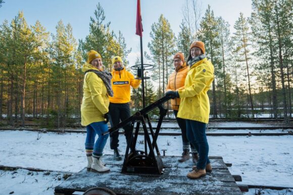 iloisia henkilöitä keltaisissa takeissa resiinan kyydissä lumisessa maisemassa