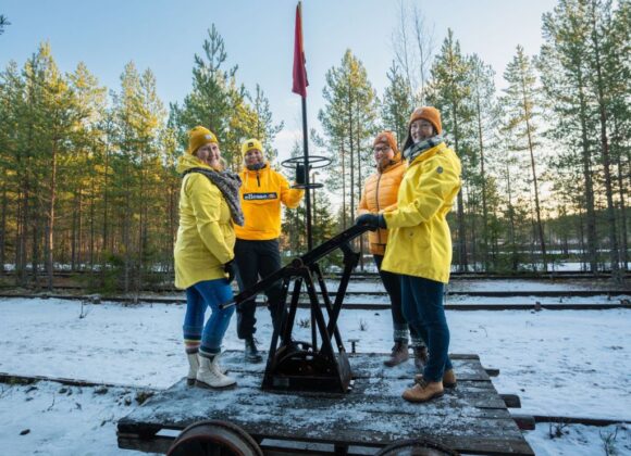 iloisia henkilöitä keltaisissa takeissa resiinan kyydissä lumisessa maisemassa