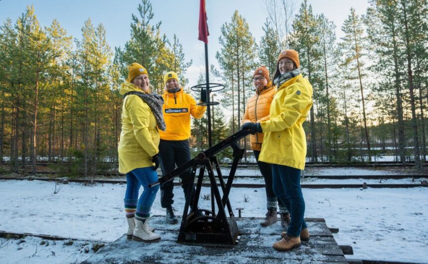 iloisia henkilöitä keltaisissa takeissa resiinan kyydissä lumisessa maisemassa